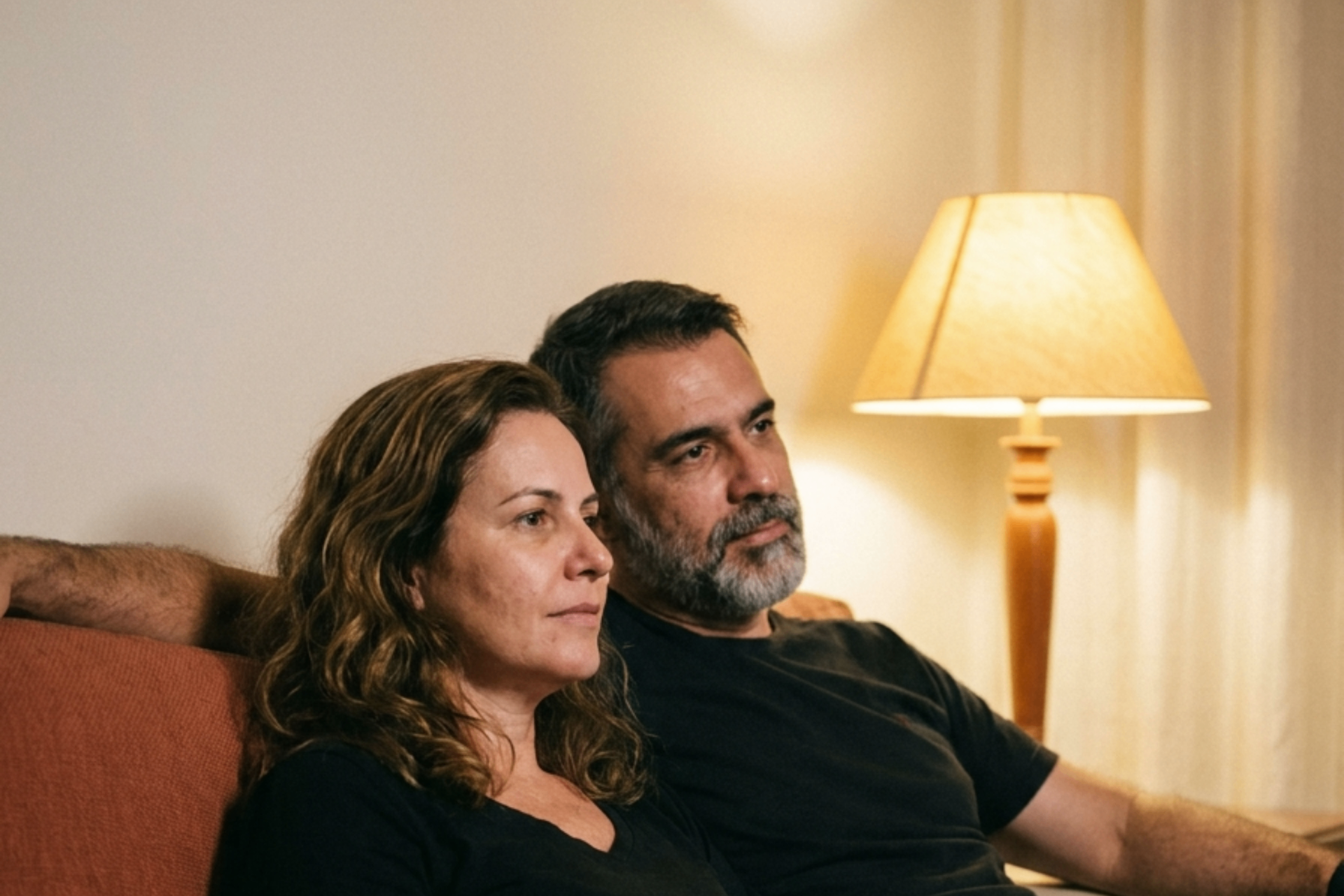Casal maduro no sofá à noite, luz quente do abajur, presença tranquila entre os dois